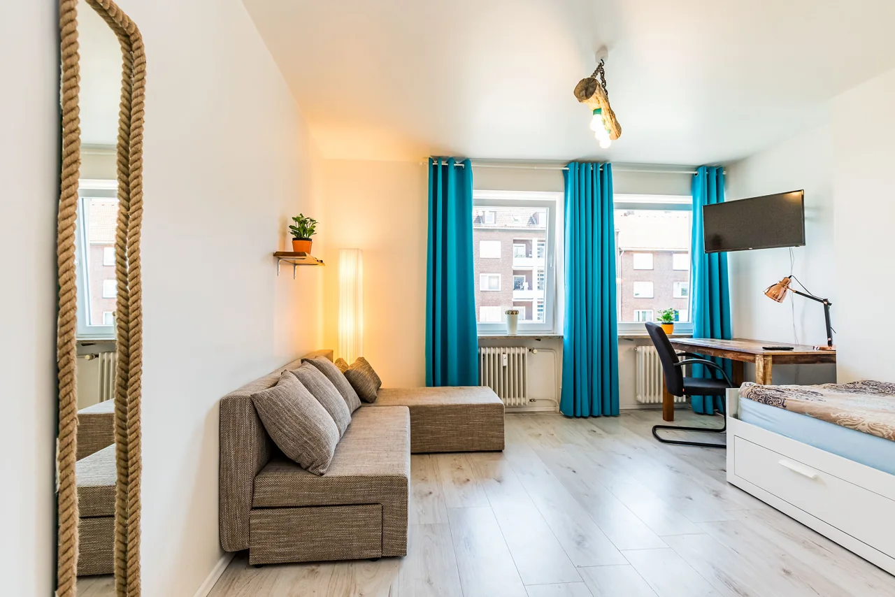 Helles möbliertes Zimmer mit Bett, Sofa und türkisfarbenen Vorhängen am ehemaligen Standort Hoheluftchaussee